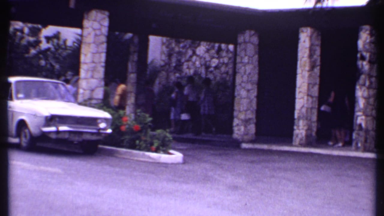 White sedan beside a stone-pillared covered walkway with people in the background.
