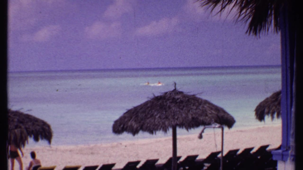 Beach with thatched umbrella, lounge chairs, pale sand, and calm sea.