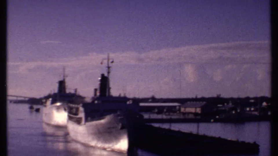 Bahamas harbor scene with a docked ship, pier structures, calm water, and hazy sky in 1969 home-movie footage.