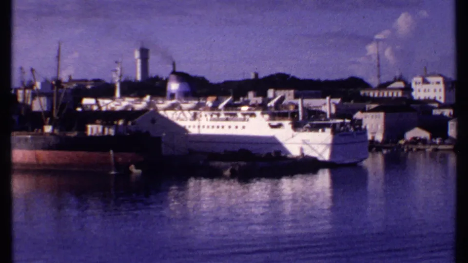 1969 Bahamas harbor frame with the passenger ship closer to center, cargo vessel at left, and industrial buildings along the shore.