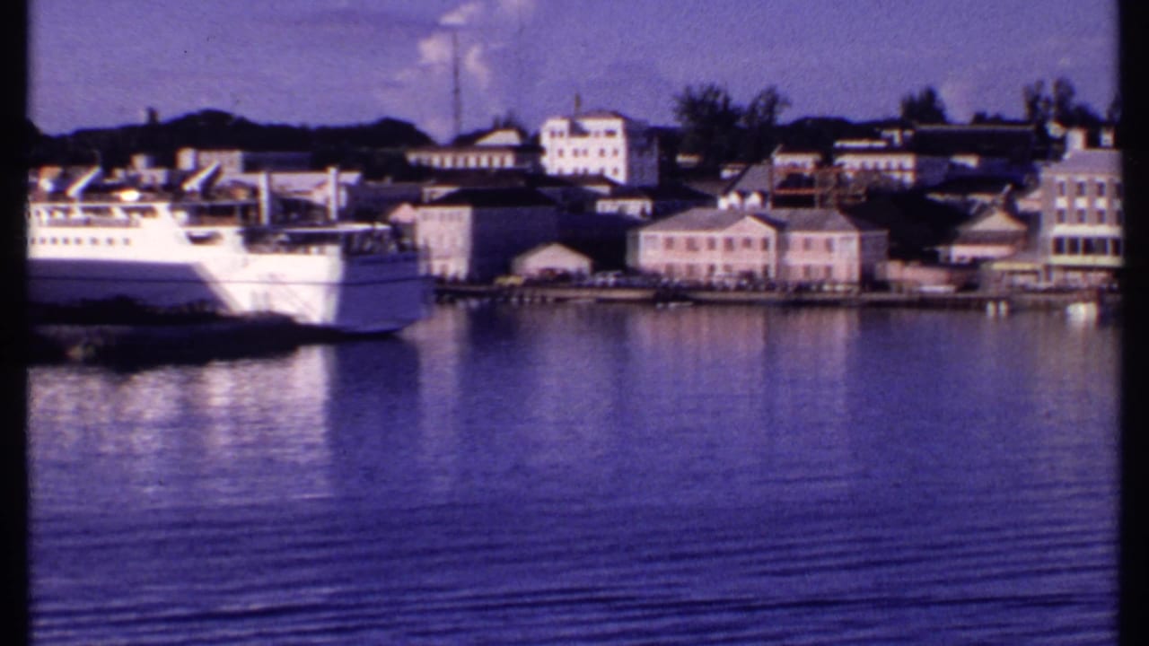 White ferry docked beside a calm harbor with waterfront buildings across the water.