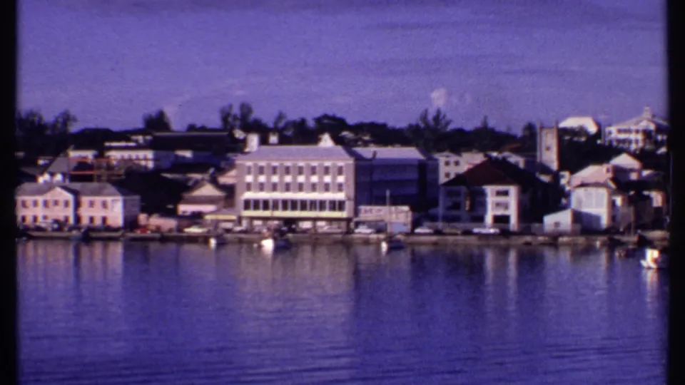 Bahamas harbor panorama ending on colonial-style shoreline buildings, moored small boats, and a broad expanse of blue water.