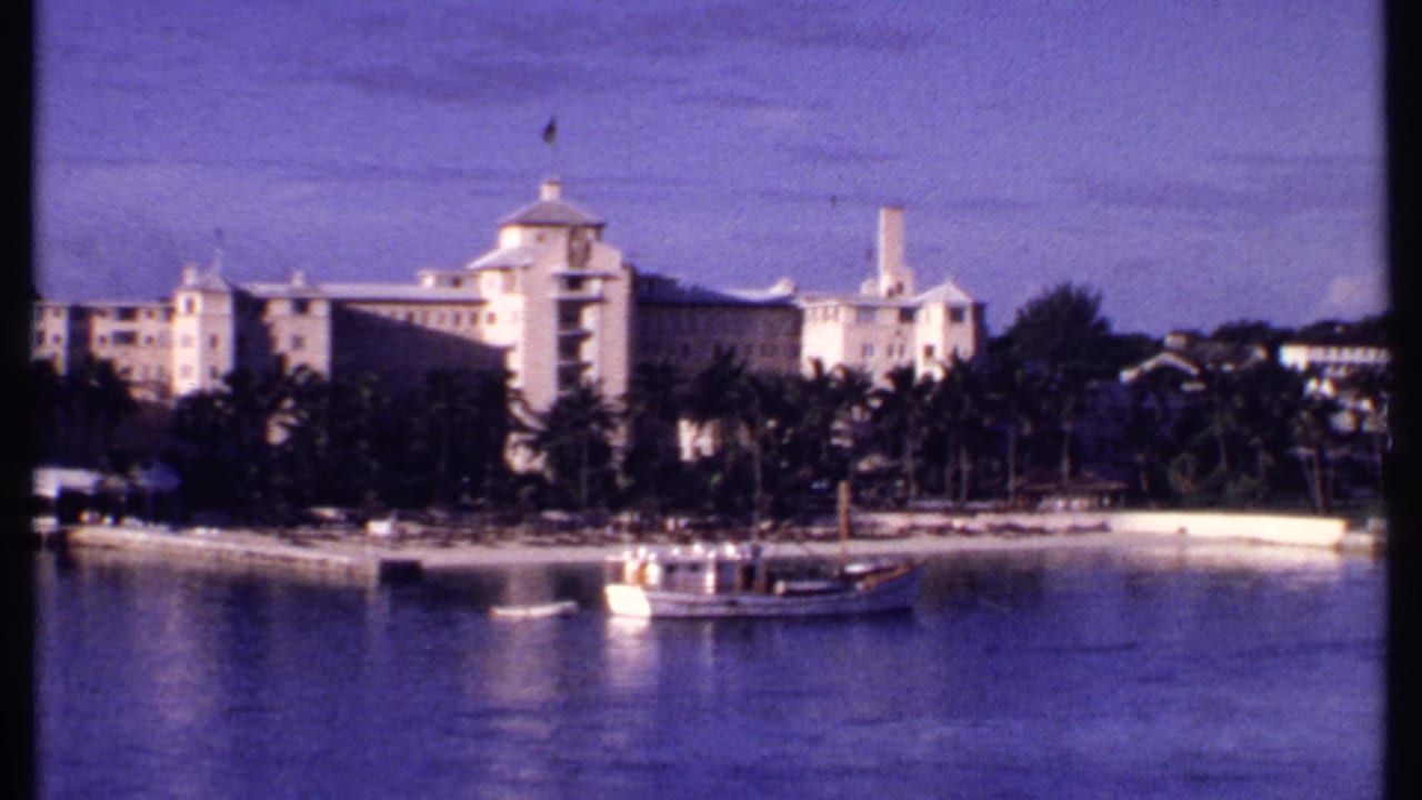 1969 Bahamas frame showing a palm-lined waterfront, resort-scale buildings, small boats, and calm bay water.