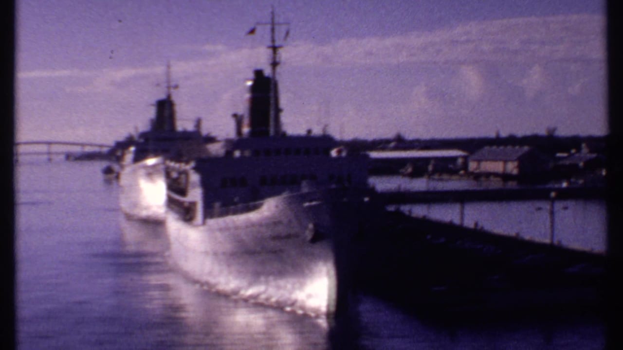 White steamers and pier viewed across still harbor water.