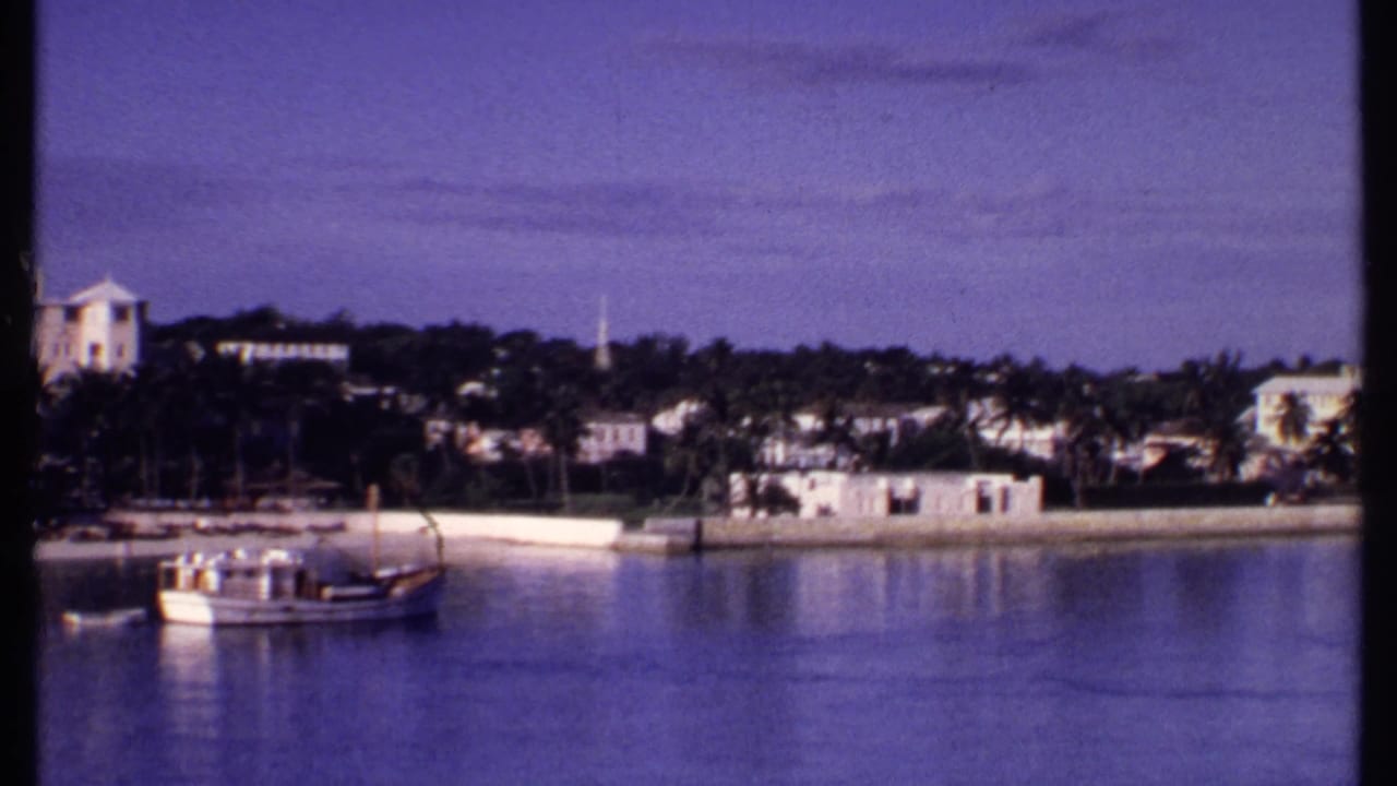 Small boat on calm water before a palm-lined shoreline with white buildings and a church steeple.