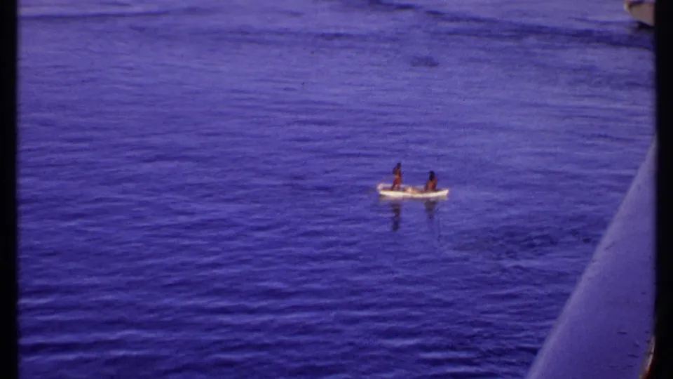 1969 Bahamas 8mm frame showing a small boat with two people on blue water, viewed from the side of a larger vessel.