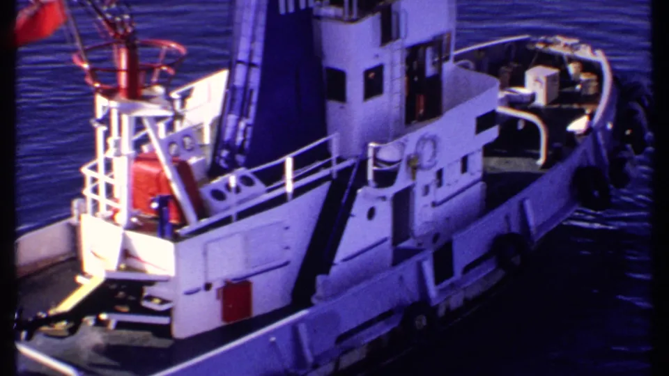1969 Bahamas 8mm view of the tugboat from above, emphasizing the cabin, red flag, railings, deck fittings, and dark funnel lettering.