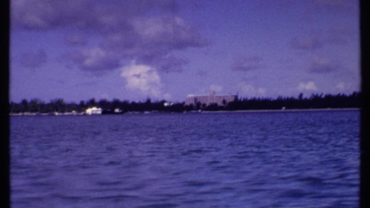 Rippling water and distant tropical shoreline under a partly cloudy sky.