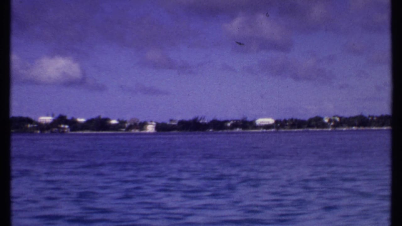 Blue water seen from a boat with a distant low shoreline and cloudy sky.