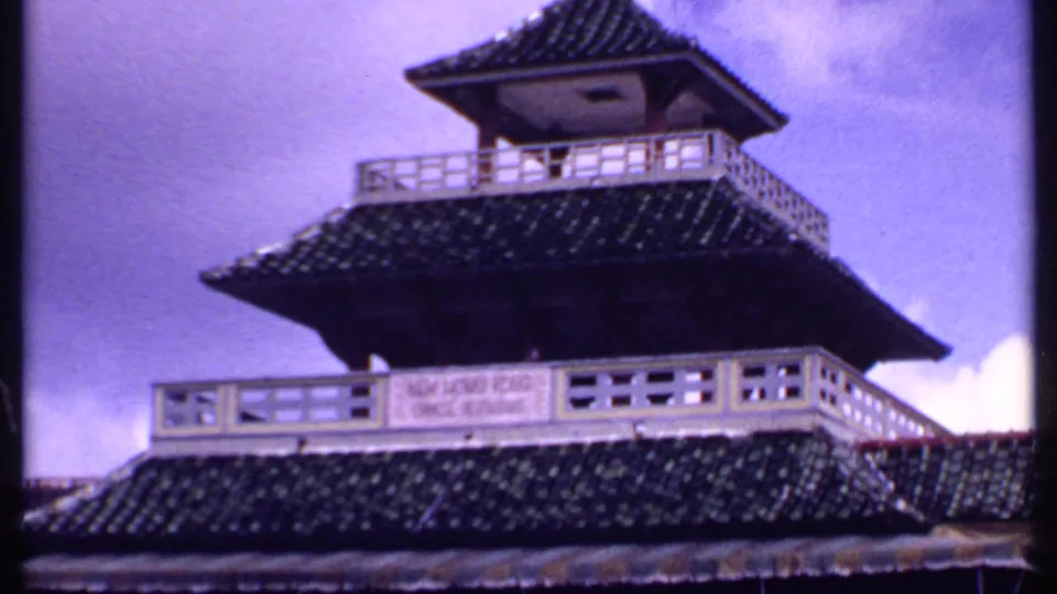 1969 Bahamas frame showing a multi-tiered pagoda-like attraction building with dark tiled roofs, white railings, and a sign panel.