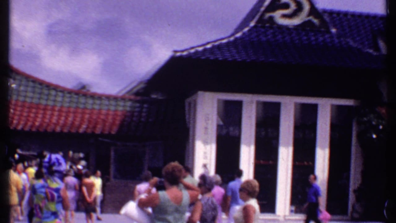 1969 Bahamas home-movie frame showing tourists outside a Chinese-style restaurant building with curved tiled roofs and white entrance panels.