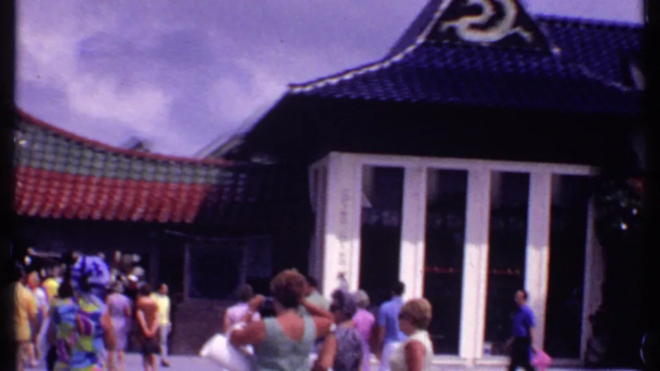1969 Bahamas home-movie frame showing tourists outside a Chinese-style restaurant building with curved tiled roofs and white entrance panels.
