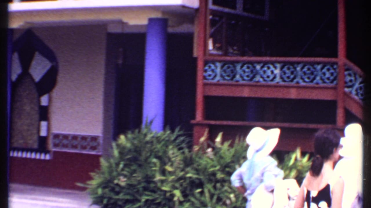 Tourists walk past purple columns and decorative railings near a market building.