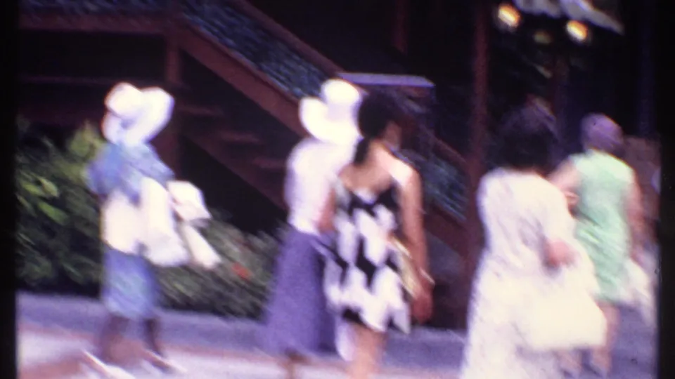 1969 Bahamas travel frame with tourists moving past a stairway and decorative railings in front of a Japanese-themed market building.