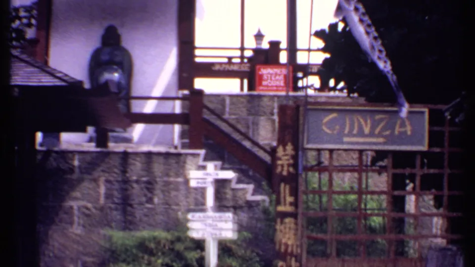 1969 Bahamas 8mm view of a Japanese-themed market entrance with GINZA signage, Japanese characters, stone steps, and a seated statue.
