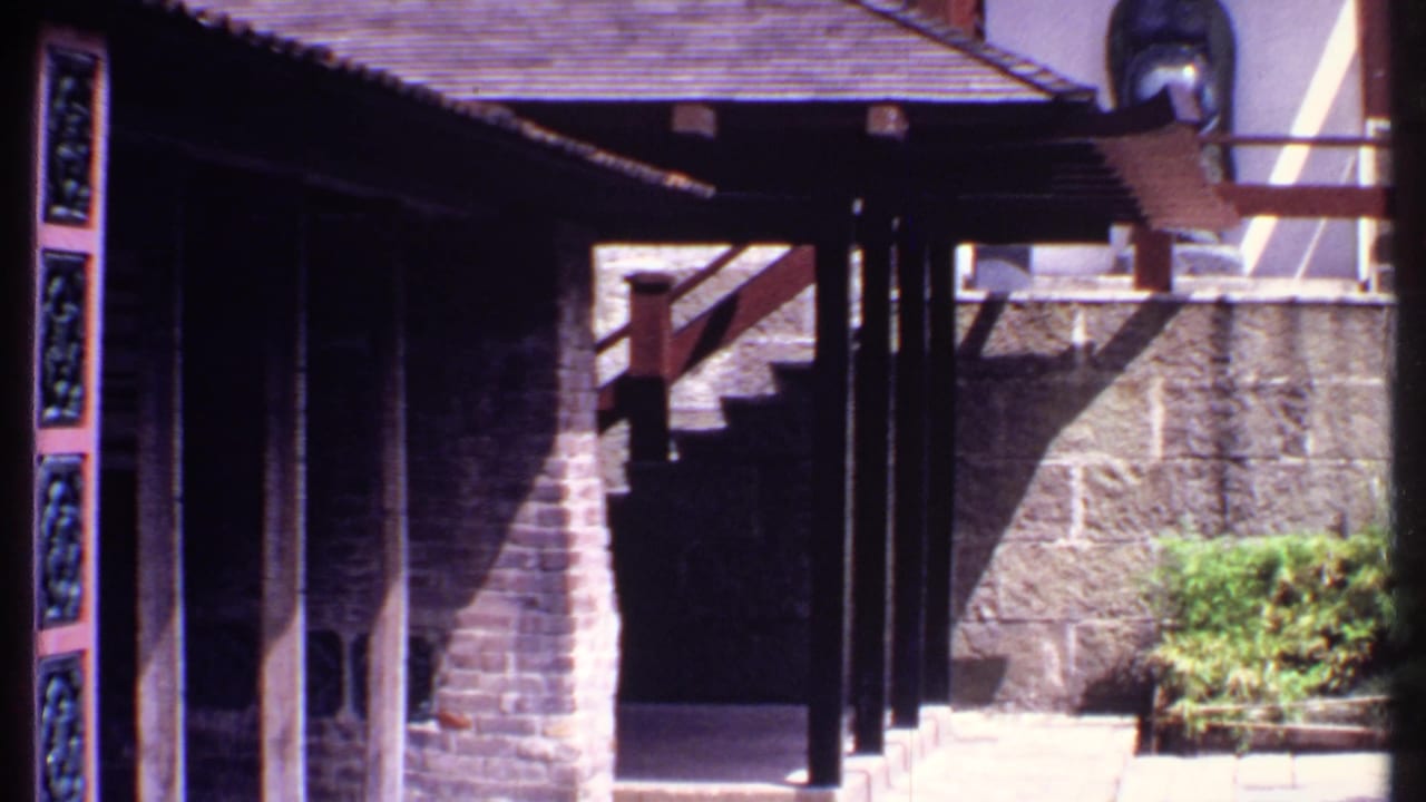 Resort walkway and stairs framed by dark wooden posts, carved blue panels, stone walls, and shrubs.