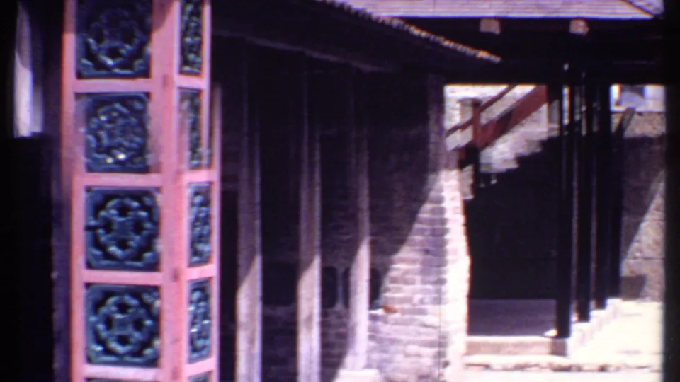 1969 Bahamas resort detail with carved blue panels, dark wooden posts, stone wall, stairs, and deep shade under the roofline.
