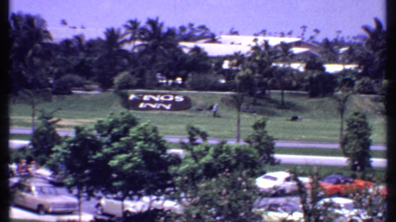 Elevated view of a Kings Inn lawn sign, palm trees, parked cars, and resort buildings.