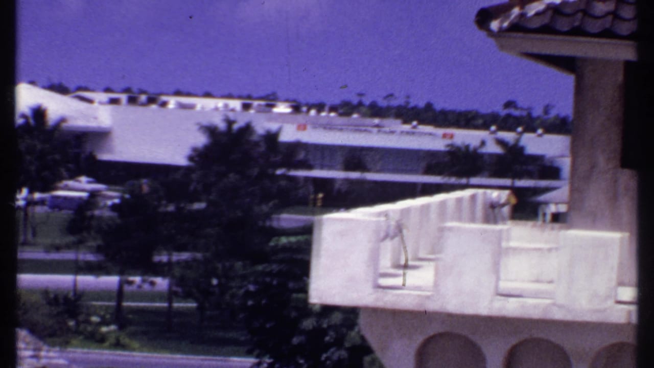 Elevated view of white buildings, trees and a road in a tropical suburban area.