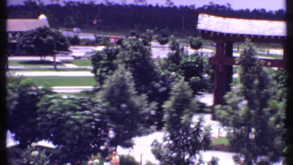 1969 Bahamas 8mm frame looking past a wooden gate structure, trees, lawns, road and distant cars.