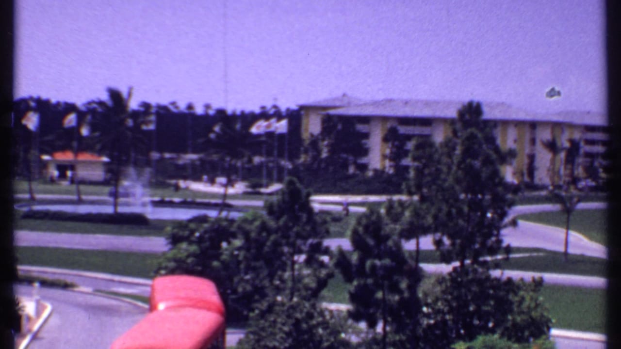 Elevated view of a resort lawn with palm trees, paths, a fountain area, and a red vehicle in the foreground.