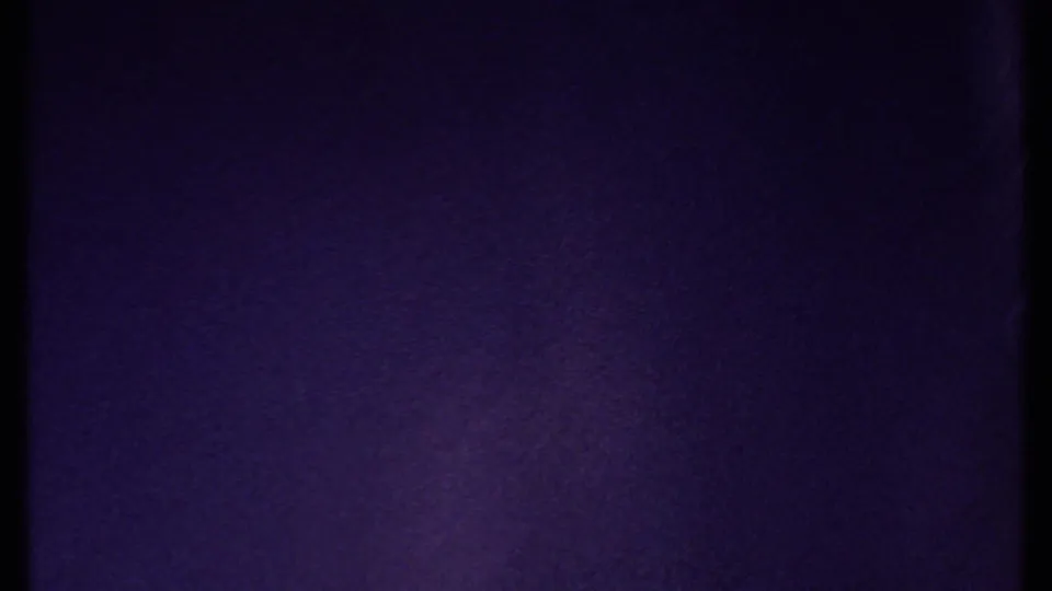 Tinted 8mm frame showing purple-blue exposure and film texture, with no identifiable subject in view.