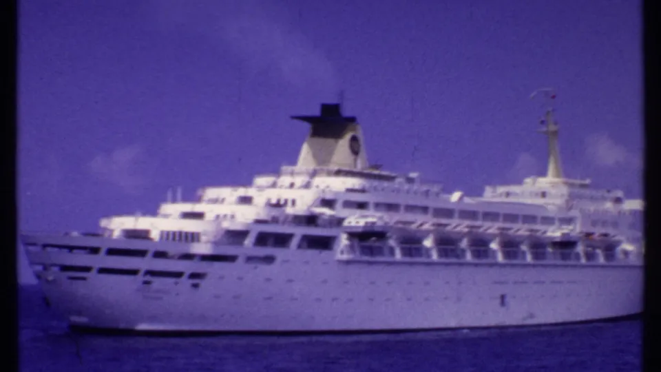 White multi-deck cruise ship on the ocean in Bahamas vacation footage, with purple-blue 8mm color shift and soft focus.