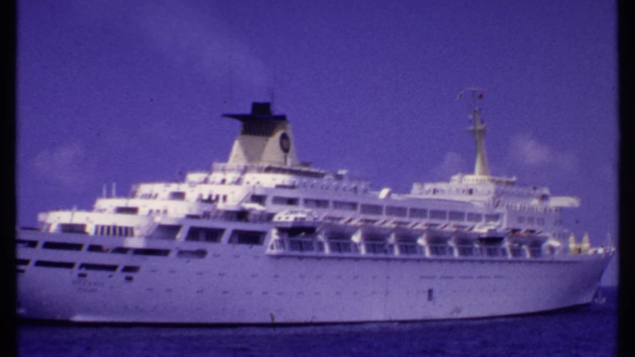 Large white cruise ship seen from the starboard side on blue water under clear sky.