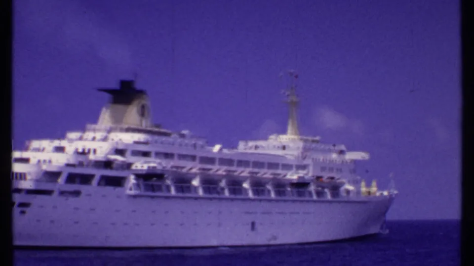 1969 Bahamas home-movie frame of a white cruise ship on calm ocean, with decks, funnel, lifeboats, and mast visible.