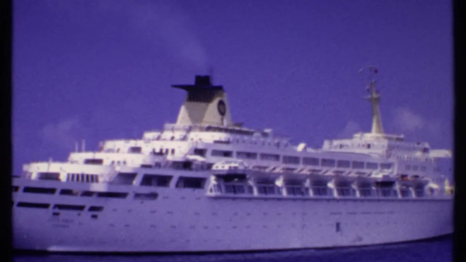 1969 Bahamas home-movie frame showing the white cruise ship filling much of the frame, with funnel, mast, decks, and ocean visible.