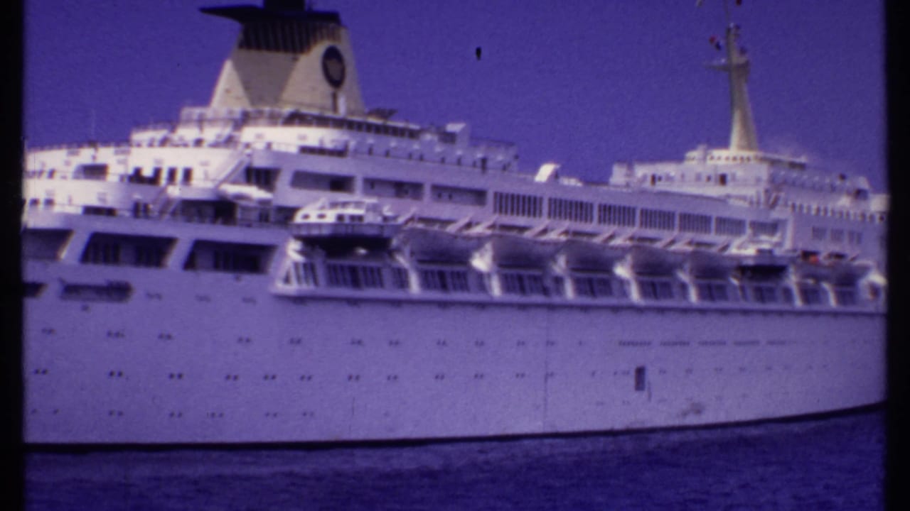 Large white cruise ship seen side-on across calm blue water.