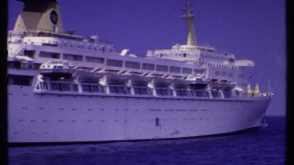 1969 Bahamas home-movie frame of a white passenger ship broadside, with lifeboats and upper decks visible against a blue sky.