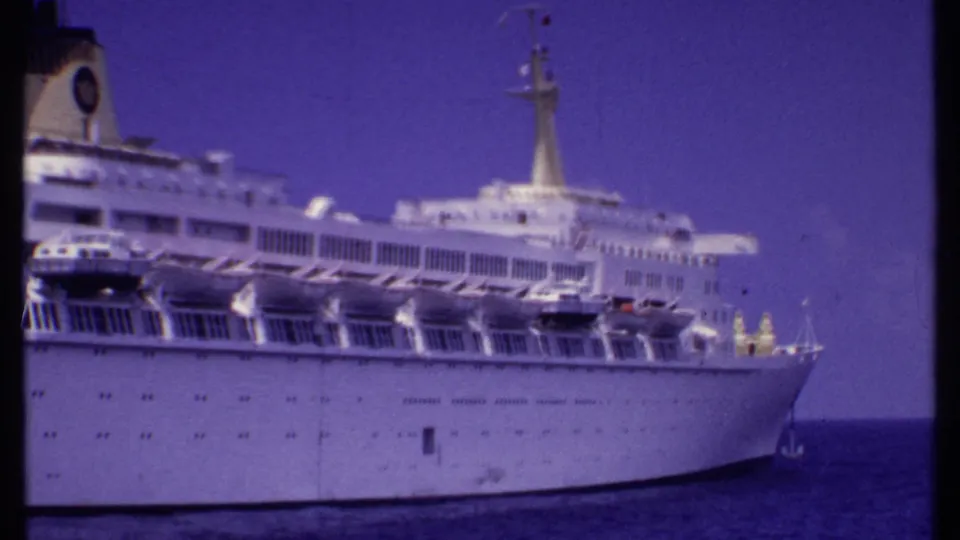1969 Bahamas 8mm frame with a closer view of the ship's bow, lifeboats, upper decks, mast, and calm ocean surface.