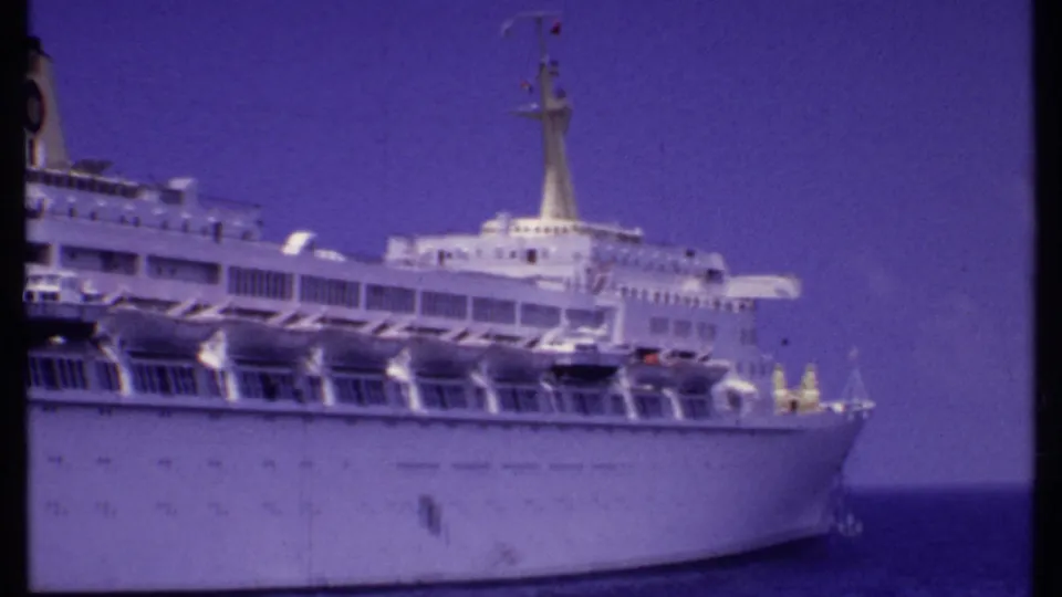 1969 Bahamas home-movie frame showing the forward section of a white cruise ship, lifeboats, mast, and blue ocean with visible film borders.