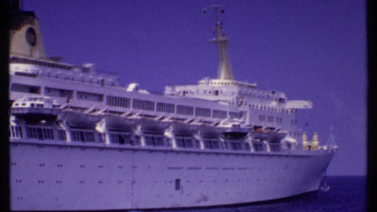 1969 Bahamas home-movie frame showing a large white cruise ship with lifeboats, decks, mast, and bow visible at sea.