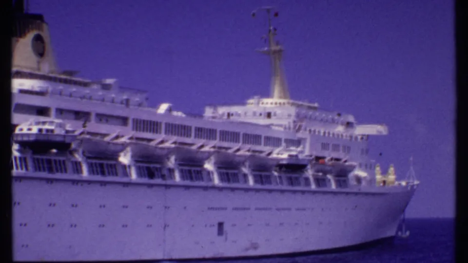 1969 Bahamas home-movie frame showing a large white cruise ship with lifeboats, decks, mast, and bow visible at sea.