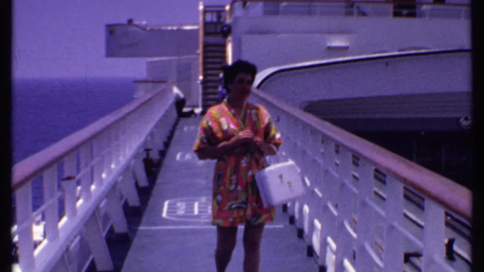 A woman in a bright patterned dress approaches the camera on a cruise ship gangway in supported 1969 Bahamas footage.