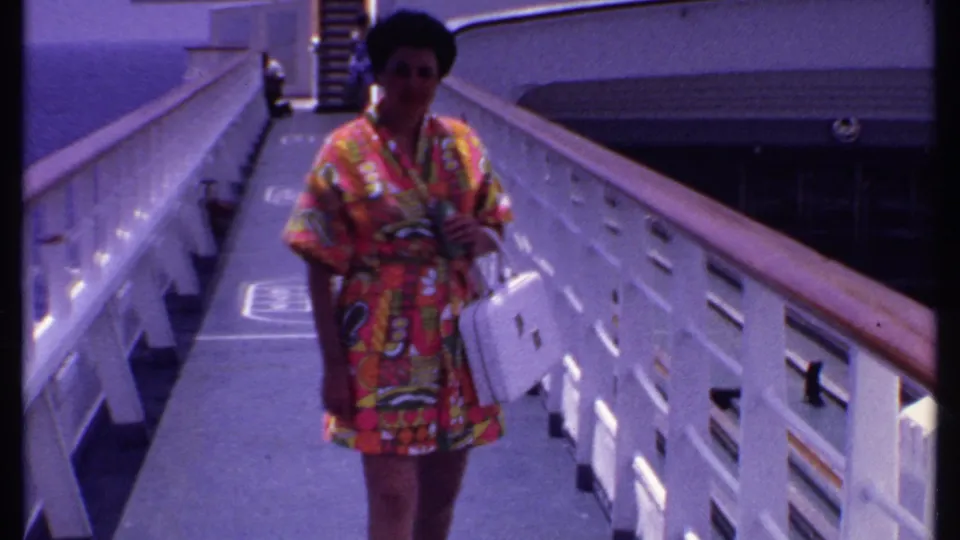 The woman continues toward the camera on the cruise ship deck, framed by white railings and deck structures in Bahamas footage from 1969.