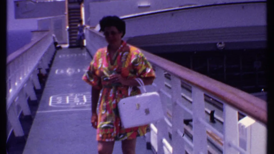 A closer 8mm frame shows the woman on the cruise deck holding a white handbag, with deck markings and railings around her.