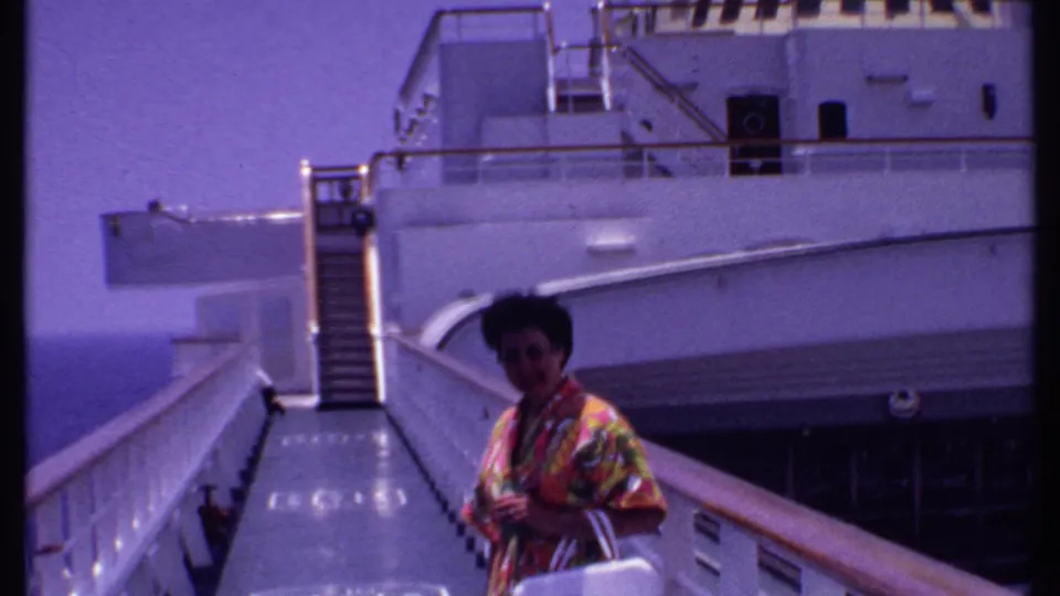 1969 Bahamas cruise home-movie frame showing a woman on a gangway with a white ship exterior and ocean visible behind her.