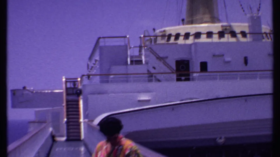 1969 Bahamas cruise footage frame with the ship side, gangway rails, stairs, and the woman partly low in frame.