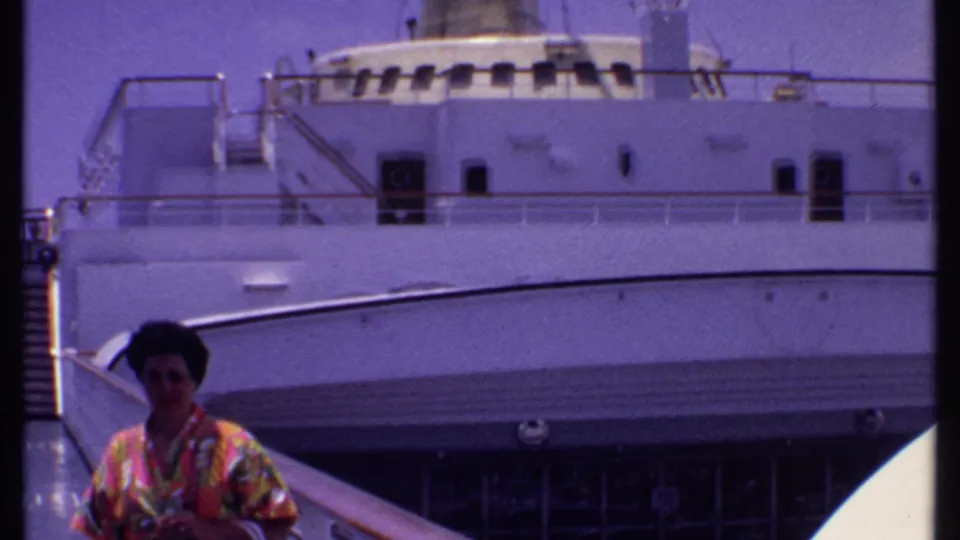 1969 Bahamas cruise home-movie frame showing a woman near the lower left of a gangway view, backed by the white ship exterior.