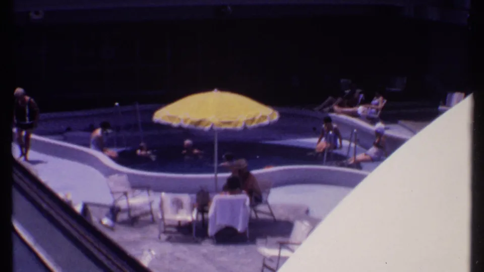 Bahamas poolside view from 1969 with swimmers, seated guests, lounge chairs, and a bright yellow umbrella.