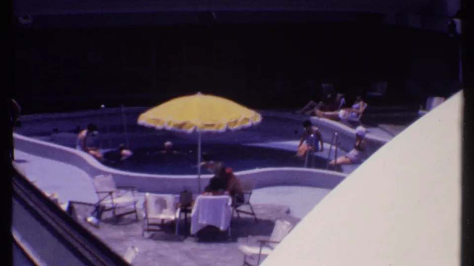 Vintage Bahamas pool scene with a yellow umbrella over the water and guests relaxing on the surrounding patio.