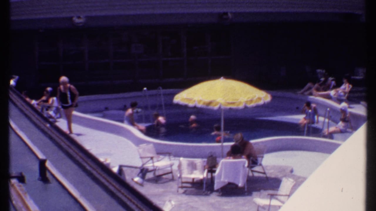 Cruise ship pool deck with swimmers, sunbathers, lounge chairs, and a yellow umbrella.