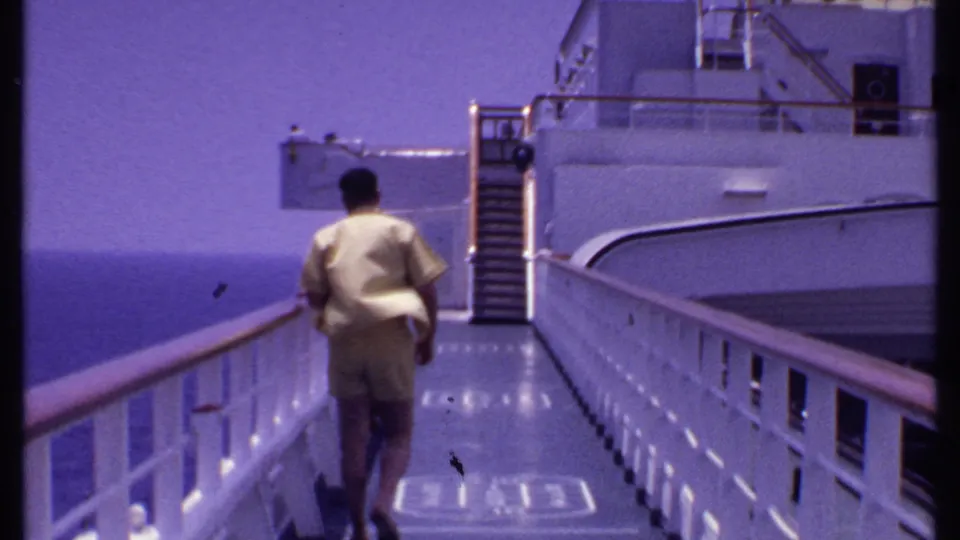 1969 Bahamas cruise frame with a man in a yellow shirt walking along a white ship deck as the ocean meets the horizon.