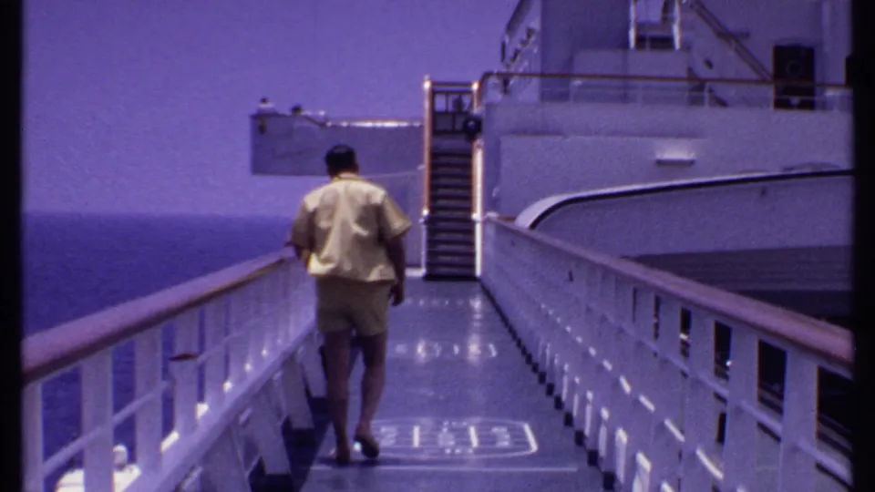 1969 Bahamas cruise footage frame showing a man from behind on a white deck, with railings, stairs, and open sea nearby.
