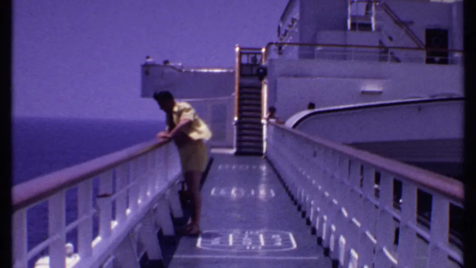 1969 Bahamas cruise home-movie frame showing a man leaning over the ship railing and looking down toward the water.
