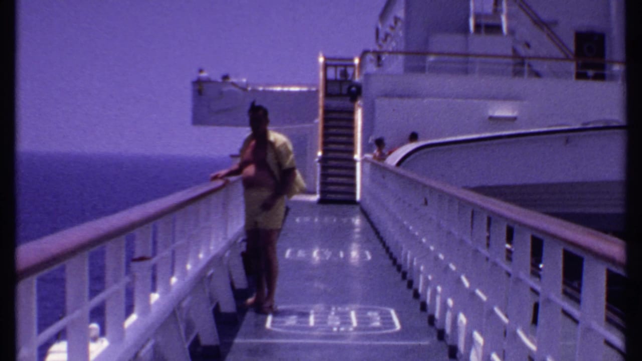 Man in yellow clothing stands by a white cruise ship railing with ocean beyond.