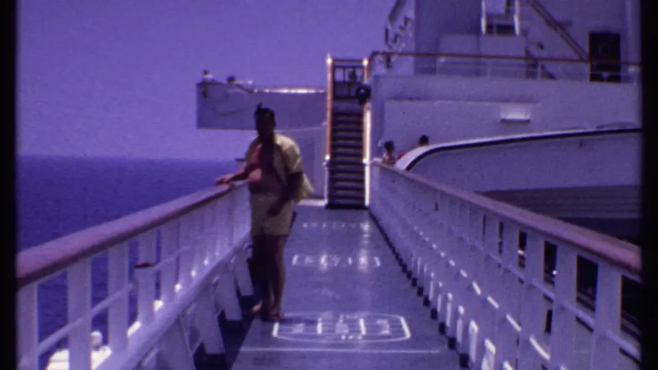 A man in a yellow outfit pauses near the railing on a Bahamas cruise ship deck in 1969, with ocean and deck stairs visible.